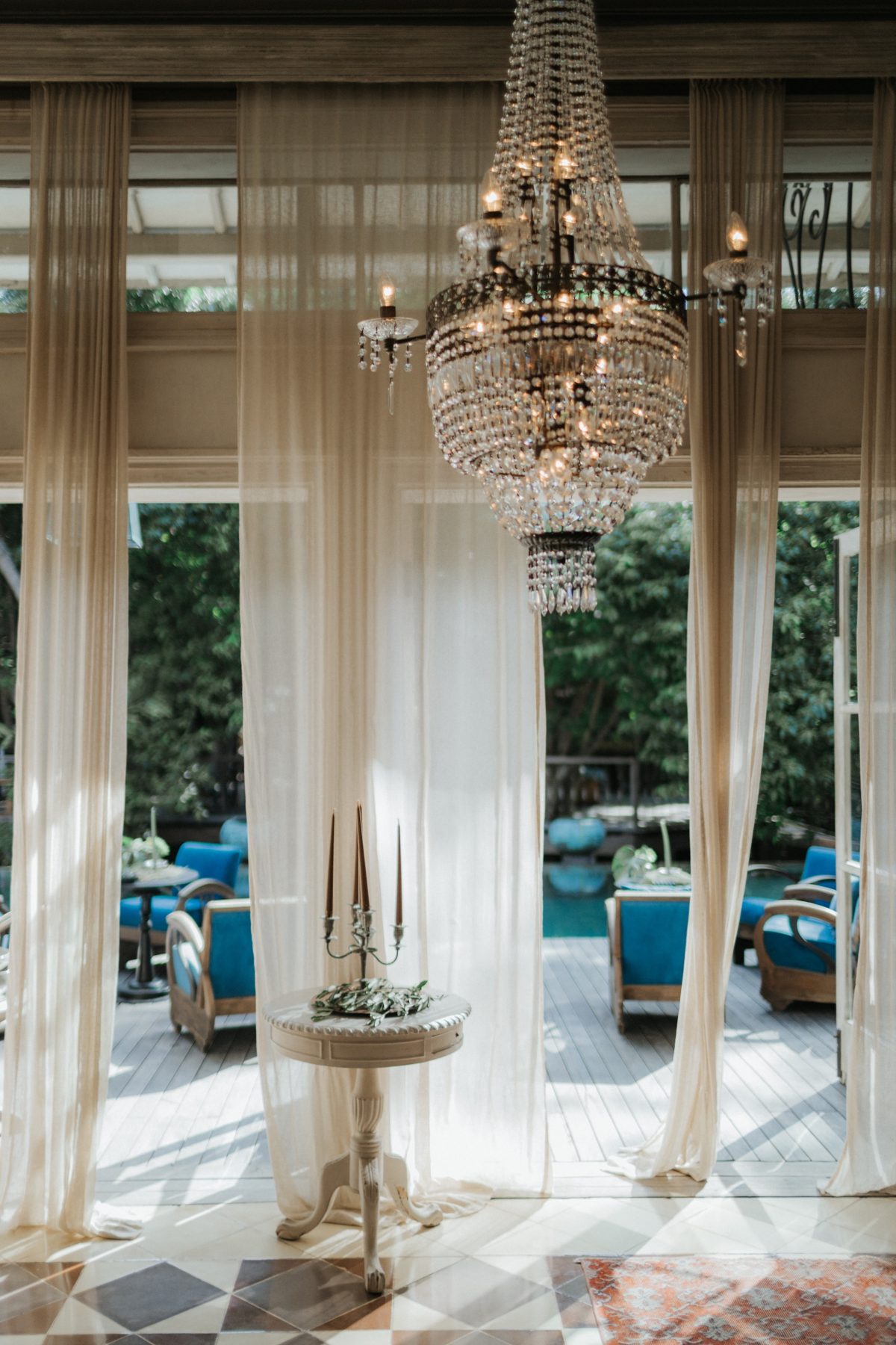 Crystal chandelier and sheer curtains opening onto a pool terrace